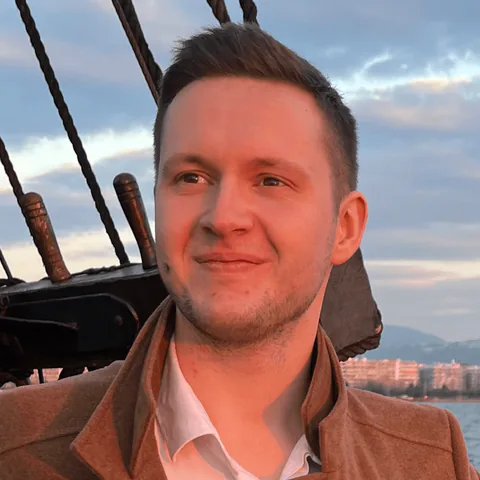 Viktar Piakarski smiling on the deck of a sailing ship at sunset